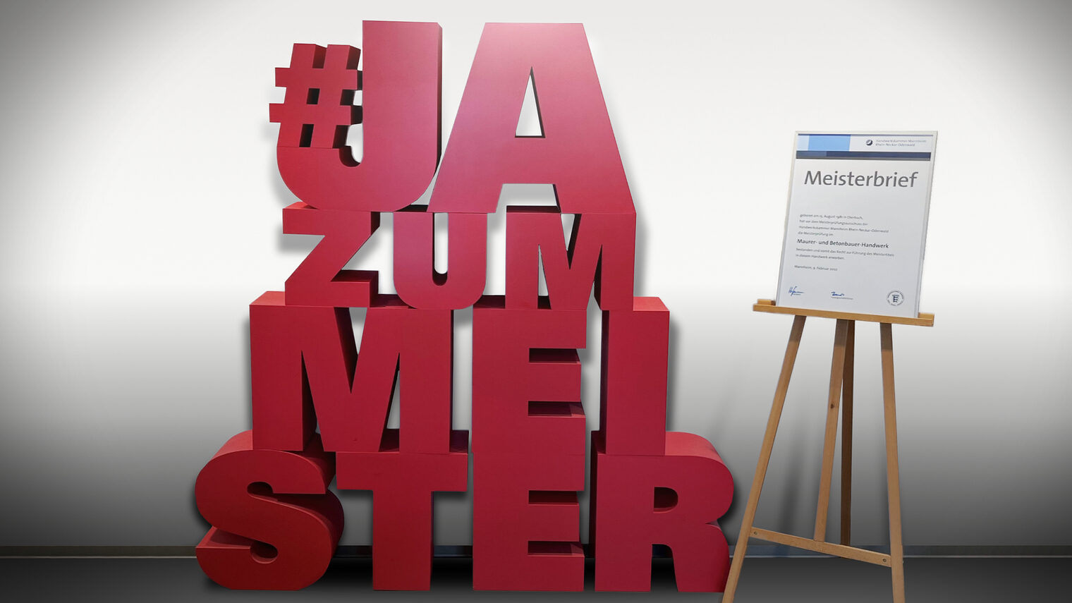Schriftzug "#JAzumMEISTER" in 3D-Optik neben einem Meisterbrief auf einer Staffelei