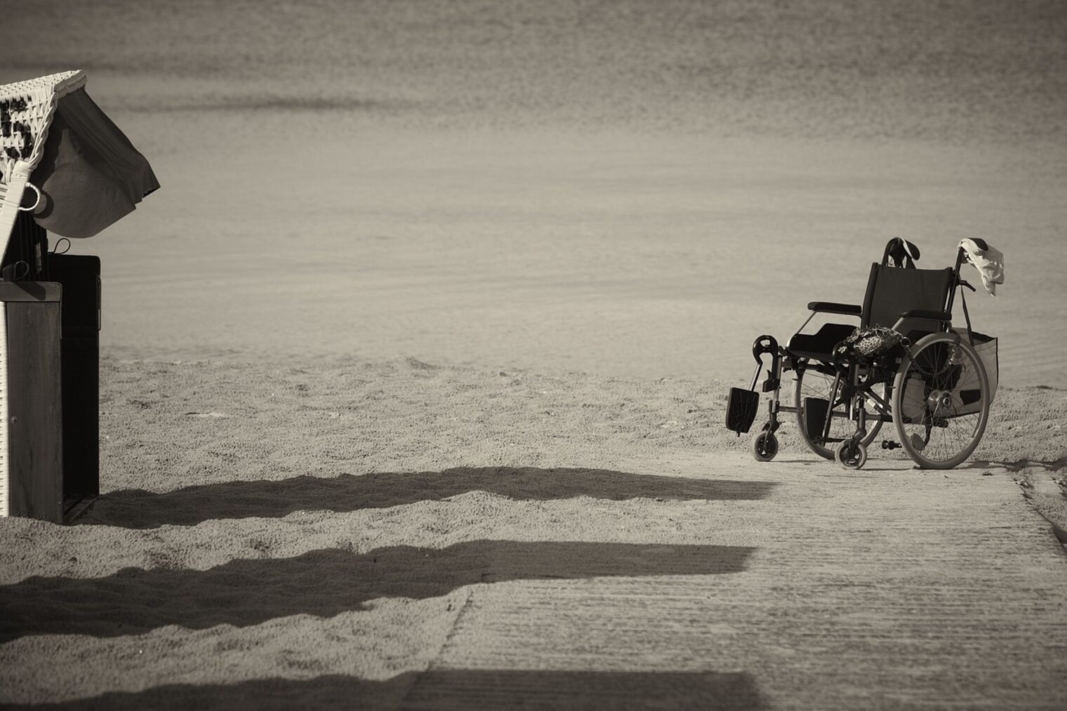 Barrierefreiheit durch einen Rollstuhl dargestellt verlassener wheelchair-Rollstuhl an einem Sandstrand neben einem Steg